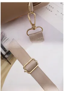 Detail of light brown leather bag featuring adjustable fabric strap and golden hardware
