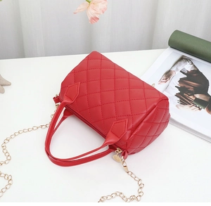 Détail du sac cylindrique matelassé rouge avec chaîne dorée et deux poignées