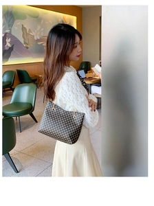 Detailed view of checkered crossbody bucket bag with elegant metal chain strap on chair