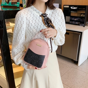 Pink and black sequined small backpack with gold metal plaque shown in a cafe setting
