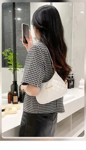 Close-up of white quilted faux leather underarm bag with gold logo on shoulder of a model