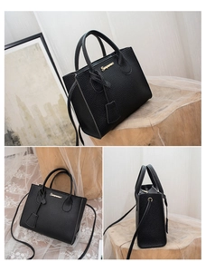 Detailed side view of black litchi pattern leather handbag with gold logo and strap