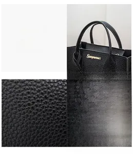 Detail of black lychee grain leather handbag showing dual handles and golden logo