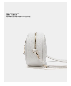 Close-up detail of white round crossbody bag with litchi texture and gold hardware