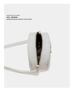 Detail of white round leather bag showing golden zipper and textured lychee pattern leather