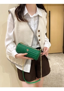 Detail of green cylinder bag with V-shaped quilting and gold chain strap on model