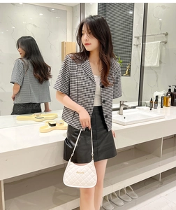 Detail of a white quilted shoulder bag paired with a houndstooth blazer and leather skirt