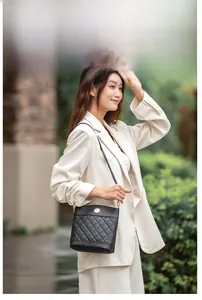 Outdoor shot of a black quilted bucket bag with a round metal buckle on a model