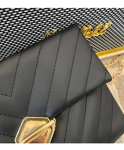 Detail of black V-quilted leather bag featuring a polished gold hexagonal twist lock