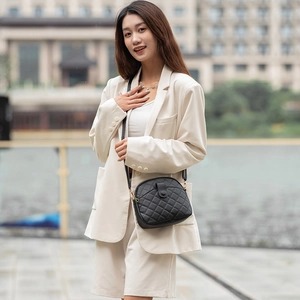 Elegant black quilted shell crossbody bag for women worn with beige suit in urban setting