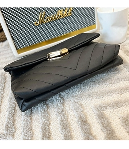 Detail of black chevron quilted leather clutch with gold rectangular clasp on a white rug