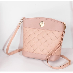 Detail of light pink crossbody bag featuring quilted diamond pattern and gold metal emblem