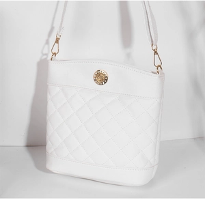 Detail of white quilted bucket bag featuring a gold metal emblem with white crystals