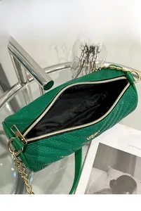 Detail view of the deep green quilted cylinder bag showing internal storage and golden chain