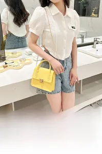Detail showing a yellow crocodile texture handbag with gold chain strap on a white top