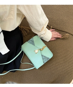 Détail du sac bandoulière vert menthe avec texture lézard et pendentif chat doré