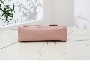 Détail du bas du sac rose à motif crocodile posé sur une surface de marbre