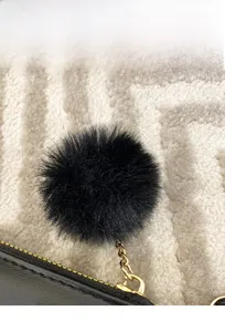 Detail of a soft black wool ball pendant accessory attached to a long leather wallet