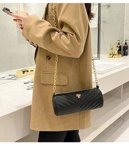 Detail of black chevron quilted cylinder bag with gold chain strap worn by a model