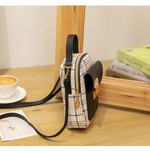 Mini beige plaid crossbody bag with black leather flap and golden hardware on wooden table