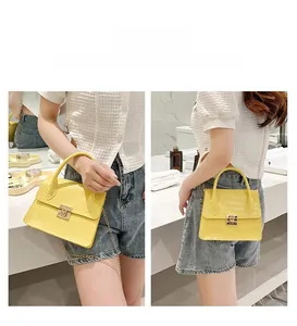 Detail of yellow crocodile pattern handbag showing metal chain strap and top handle