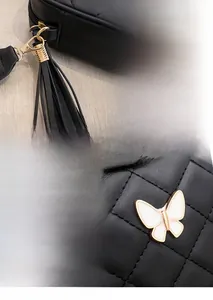 Detail of black quilted crossbody bag with gold tassel and white butterfly accent