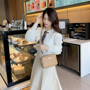 Quilted khaki crossbody bag with diamond patterns and metal logo in an urban cafe setting