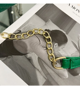 Close-up of green leather shoulder strap with bold gold metal chain and fine stitching