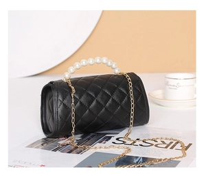 Détail du sac cylindrique noir matelassé avec poignée en perles et chaîne dorée