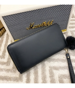 Close-up of black leather long wallet with gold zipper and decorative pom-pom charm