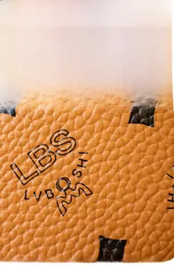 Close-up of soft brown lychee grain faux leather with logo and crown pattern detail