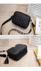 Detail of black quilted crossbody bag with stylish tassel zipper and lettered woven strap