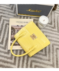 Detail of crocodile embossed yellow handbag with golden metal lock on a textured carpet