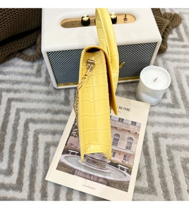 Detail of yellow crocodile embossed leather handbag with golden chain near vintage speaker