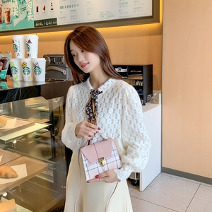 Pink plaid crossbody flap bag with gold clasp and top handle held by woman in cafe