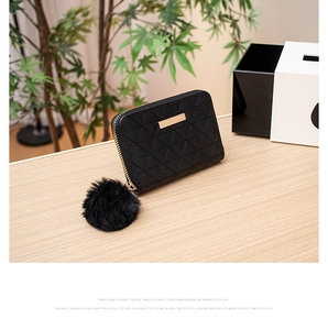 Detail of black quilted coin purse featuring a golden metal plate and soft pompom charm