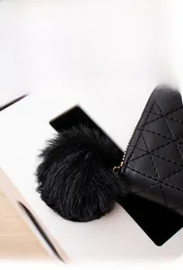 Detail of black faux fur pendant on quilted leather mini purse with metallic zipper