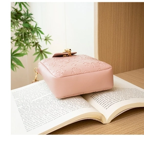 Detail of pink embossed crossbody bag with gold zippers on an open book in a warm setting