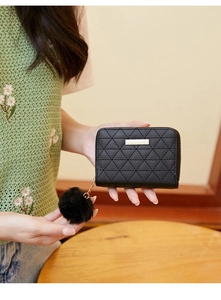 Detailed view of black quilted mini purse with gold metal bar and soft pompom charm