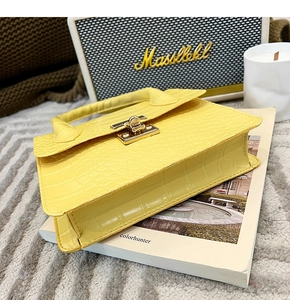 Close-up of bright yellow crocodile embossed handbag with golden twist lock on a book