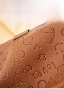 Close-up of brown leather bag with embossed bicycle, star, and heart patterns