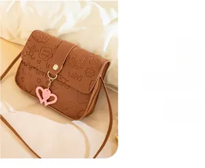 Detail of brown embossed crossbody bag with cartoon patterns and heart pendant