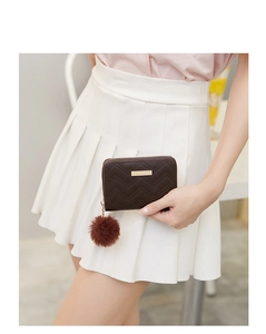 Detail of dark brown quilted wallet with a soft pompom charm and gold metal zipper