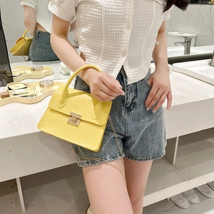 Yellow crocodile embossed mini square bag with gold lock and chain strap on a vanity tray