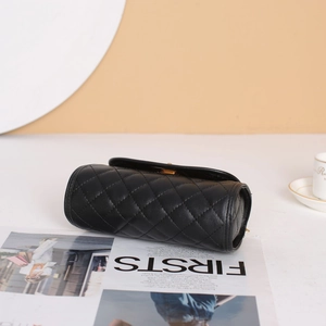 Quilted black cylinder handbag with pearl handle and gold twist lock on white surface