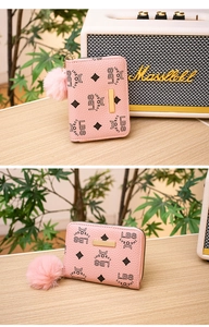 Close-up of pink faux leather zip wallet with monogram pattern and plush pompom charm