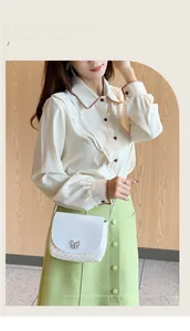 Detailansicht einer weißen Umhängetasche mit Schmetterlingslogo und modischem Outfit