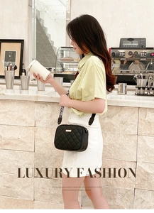 Detail of black quilted leather camera bag with golden logo and wide lettered strap