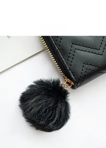 Detail of black quilted leather coin purse with golden zipper and faux fur pompom charm