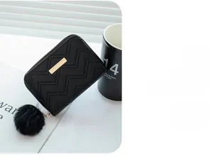 Detail of black wave-quilted mini wallet with gold hardware and faux fur pompom charm